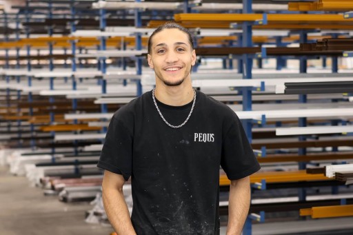 Amran Alsoboh Junger Mann in schwarzem T-Shirt mit Schriftzug vor Regalen in einer Werkstatt