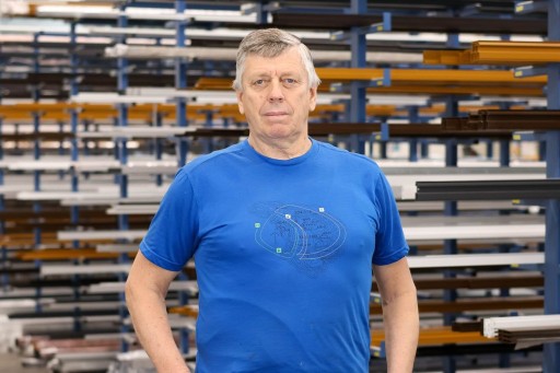 Alexander Dubovoj Ein Mann in blauem T-Shirt steht in einem Lager vor Regalen mit Metallstangen.