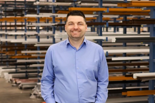 Daniel Klein Mann in blauer Hemd steht lächelnd in einer Werkstatt mit Regalen