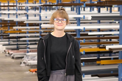 Martyna Konieczna Person mit Brille in industriellem Umfeld vor Regalen