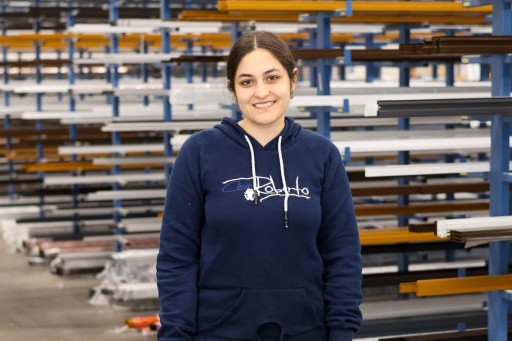 Negin Saberi Junge Frau in blauer Kapuzenjacke lächelnd vor industriellem Hintergrund