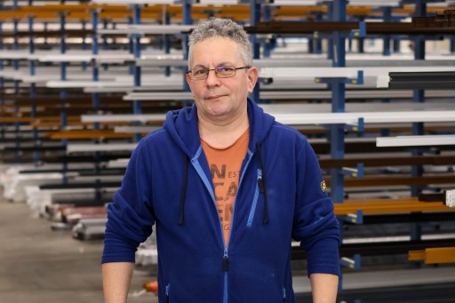 Simon Ernst Arbeiter in einer Werkstatt mit blauem Oberteil vor Metallgestellen